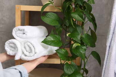 Photo of Woman putting rolled towels onto shelf indoors, closeup