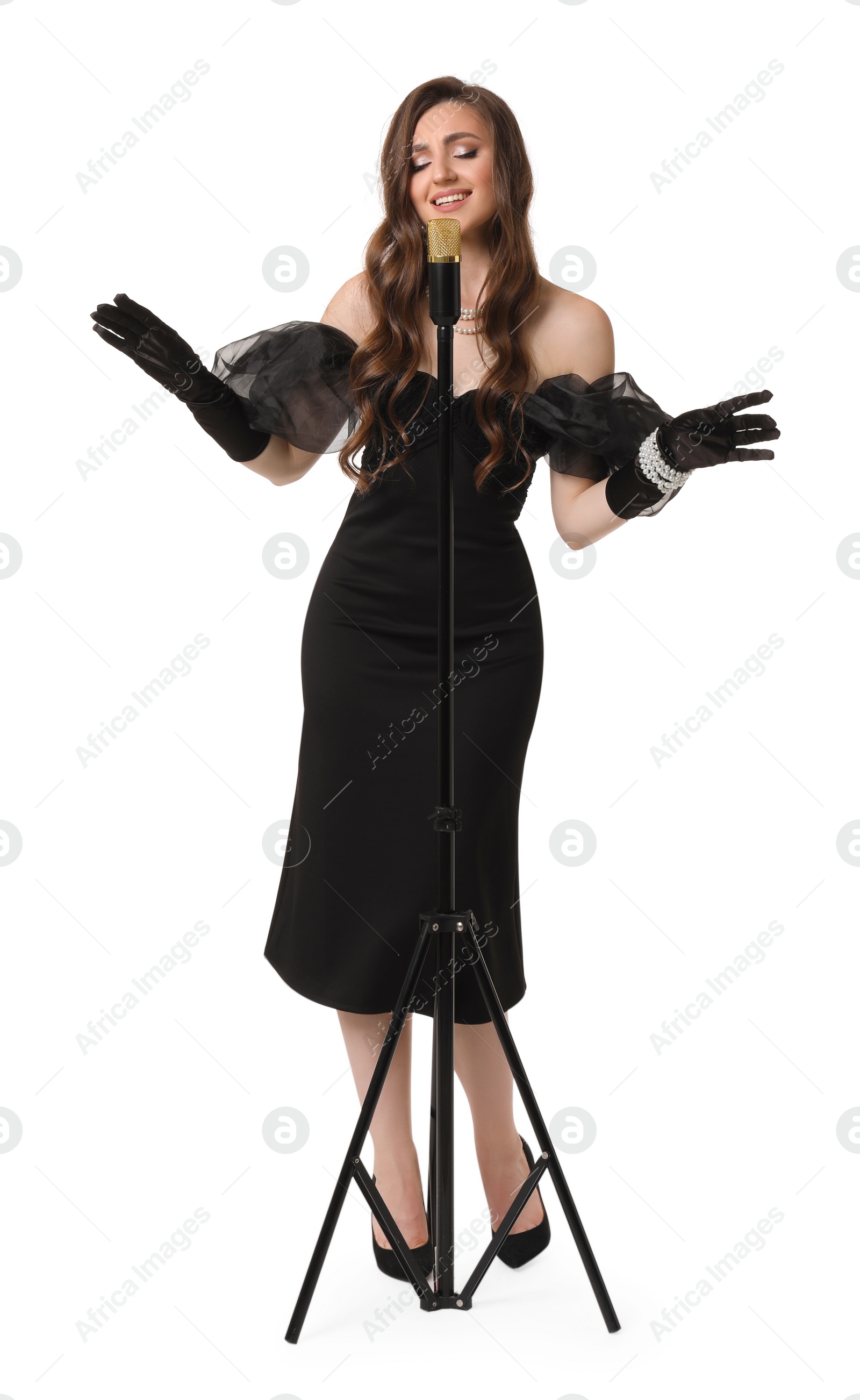 Photo of Beautiful young woman in stylish black dress with microphone singing on white background