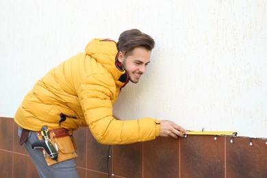 Photo of Young man measuring outdoor wall while hanging Christmas lights