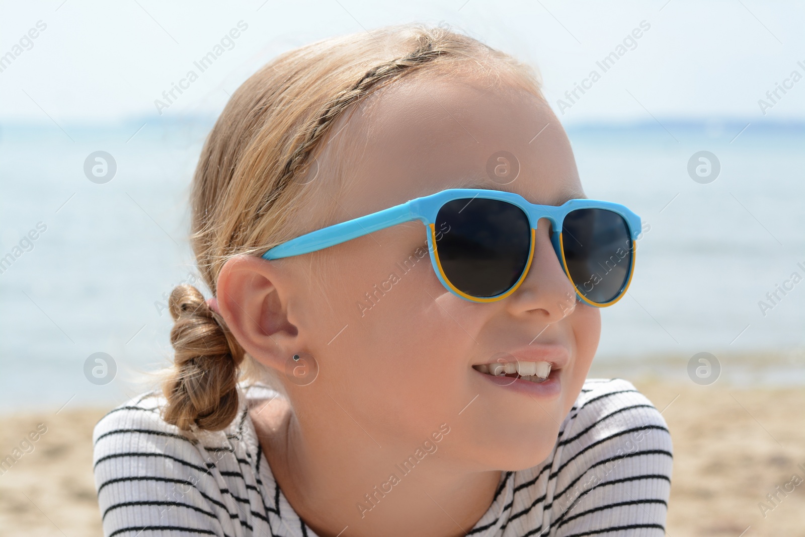 Photo of Little girl wearing sunglasses at beach on sunny day