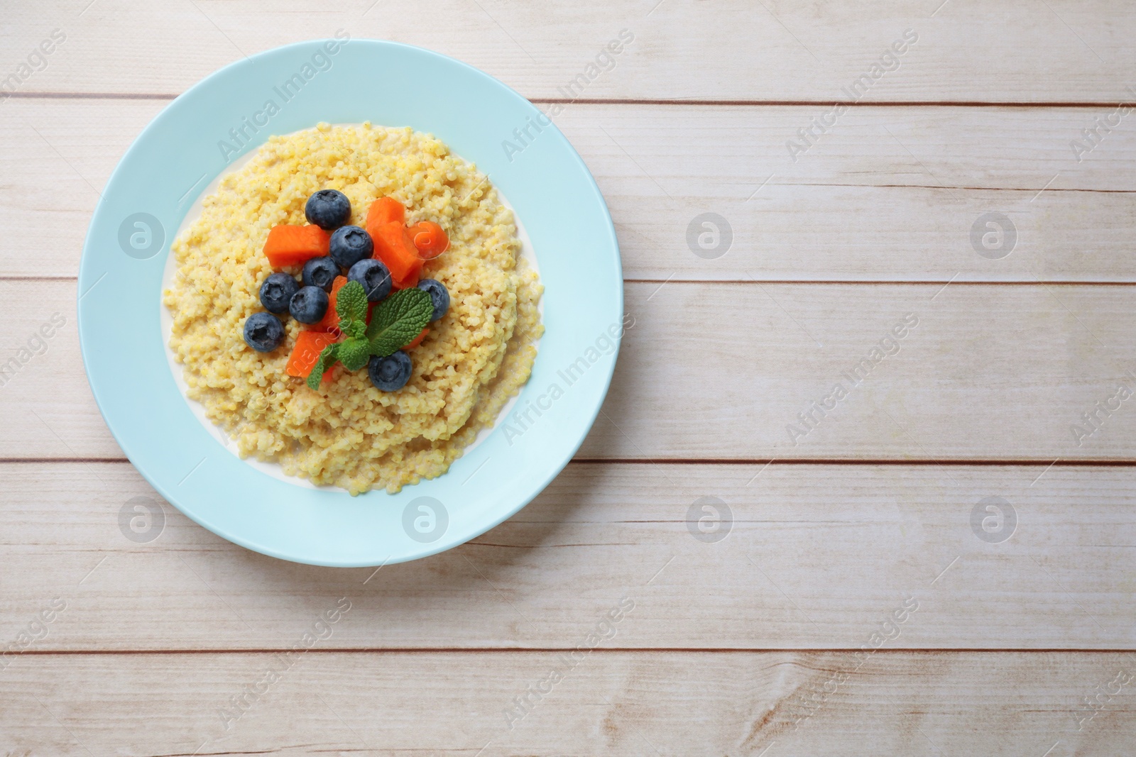 Photo of Plate with tasty millet porridge, blueberries, pumpkin and mint on light wooden table, top view. Space for text