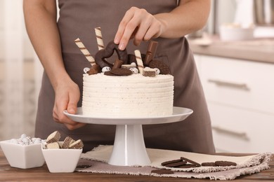 Photo of Woman decorating delicious cake with sweets at wooden table indoors, closeup