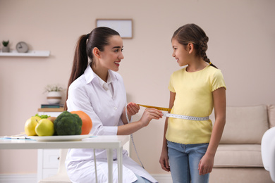 Professional nutritionist measuring waist of little girl in office