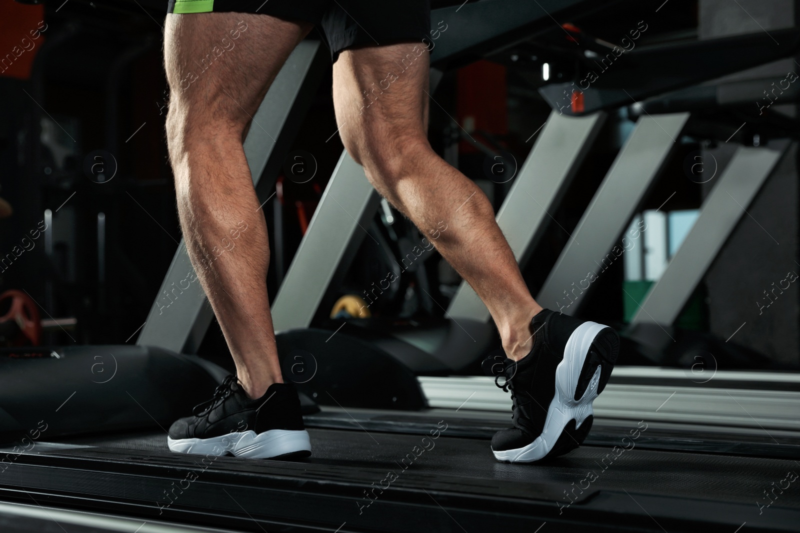 Photo of Man working out on treadmill in modern gym, closeup of legs