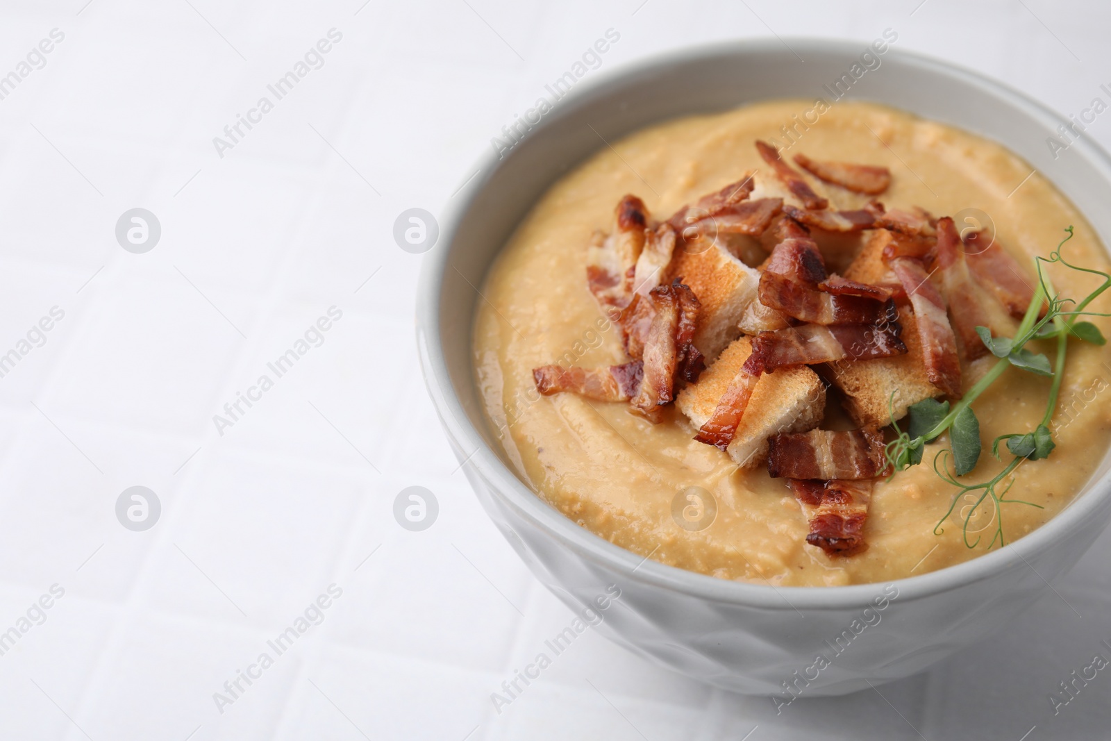 Photo of Delicious lentil soup with bacon and croutons on white tiled table, closeup. Space for text