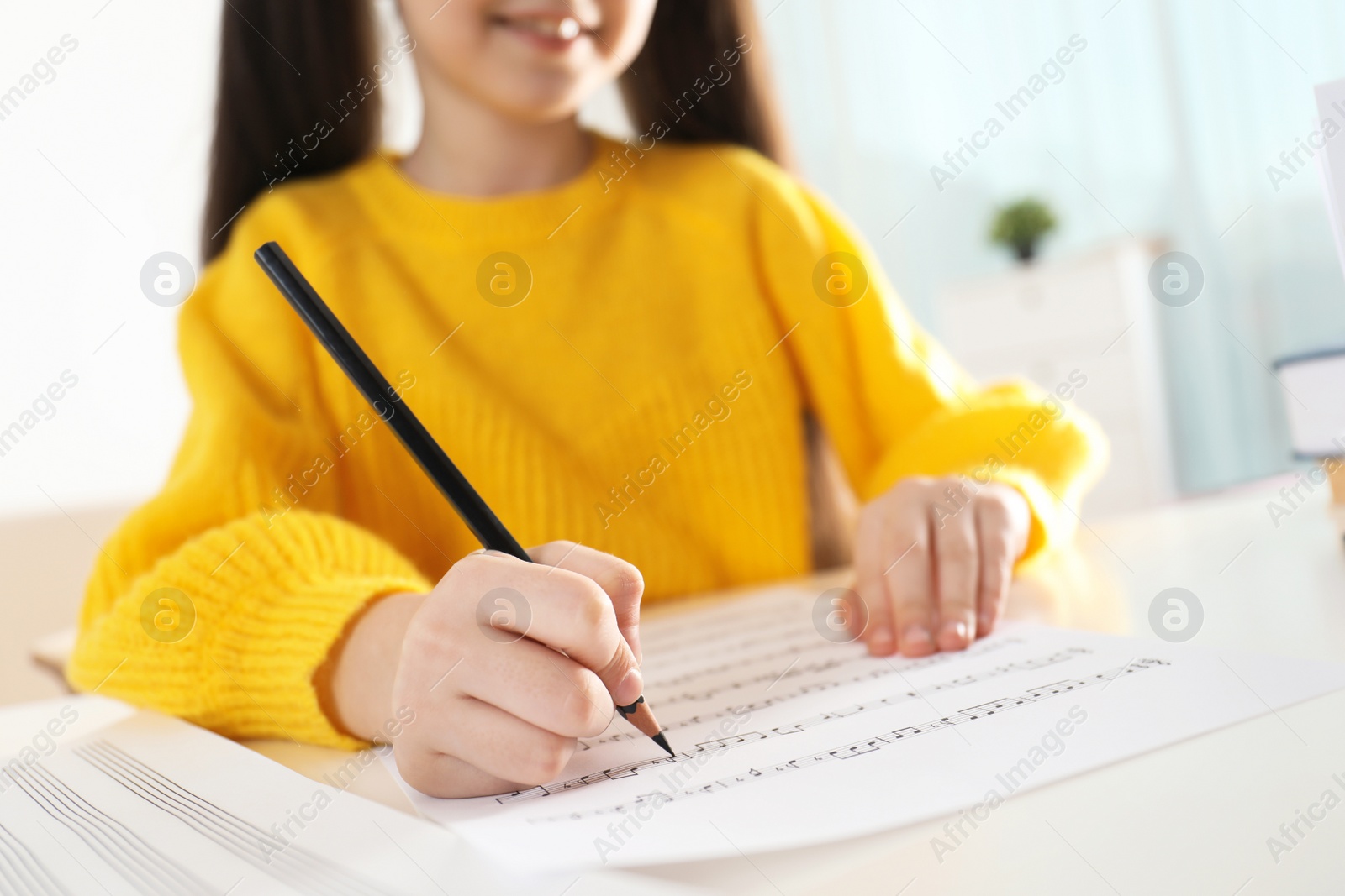 Photo of Little girl writing music notes at table, closeup