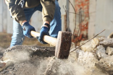 Photo of Man breaking stones with sledgehammer outdoors, closeup