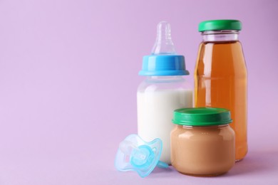 Photo of Healthy baby food, juice, milk and pacifier on lilac background, space for text