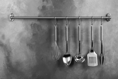 Photo of Rack with clean kitchen utensils on grey wall. Space for text