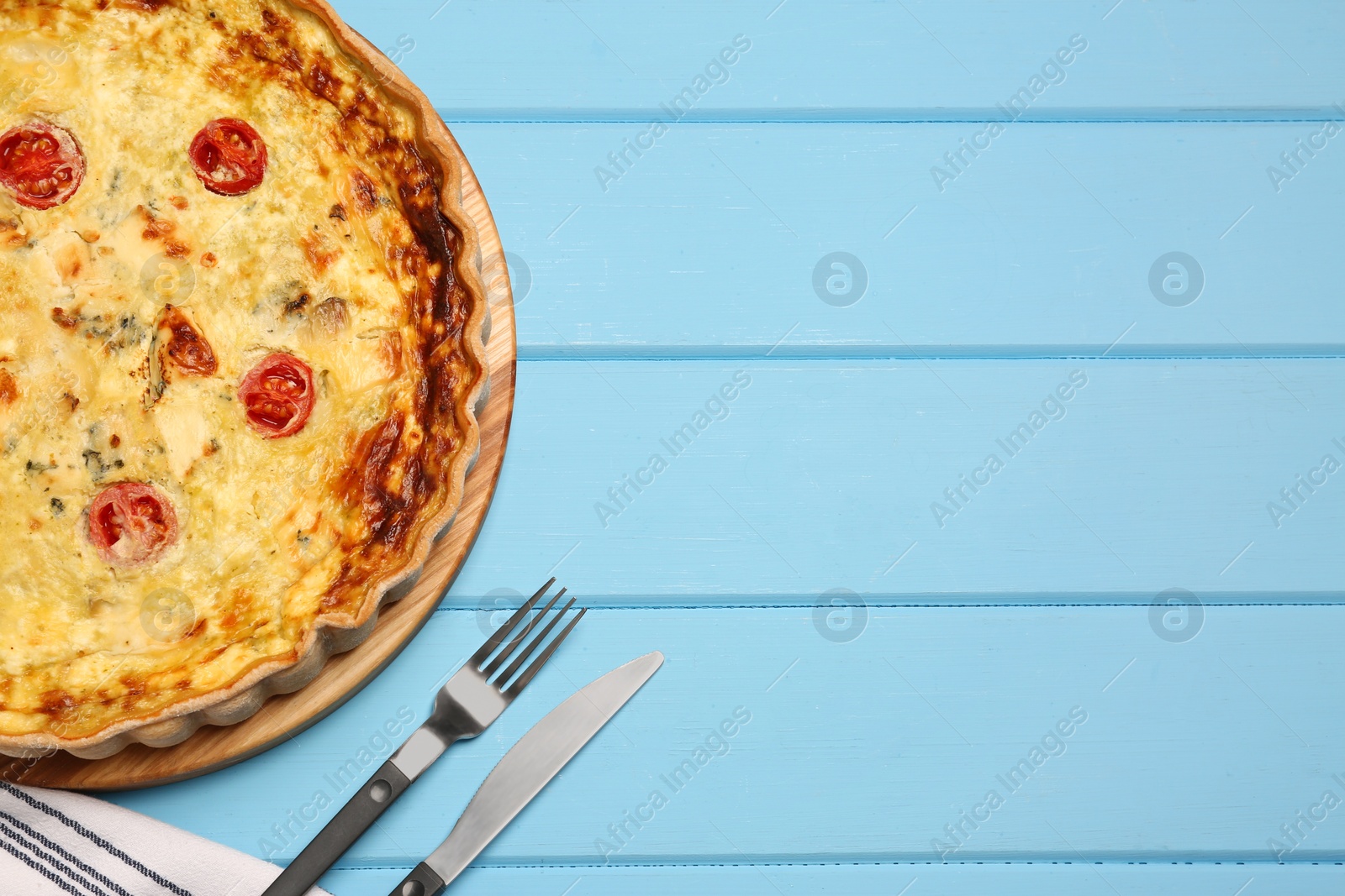 Photo of Delicious quiche with cheese and tomatoes on light blue wooden table, flat lay. Space for text