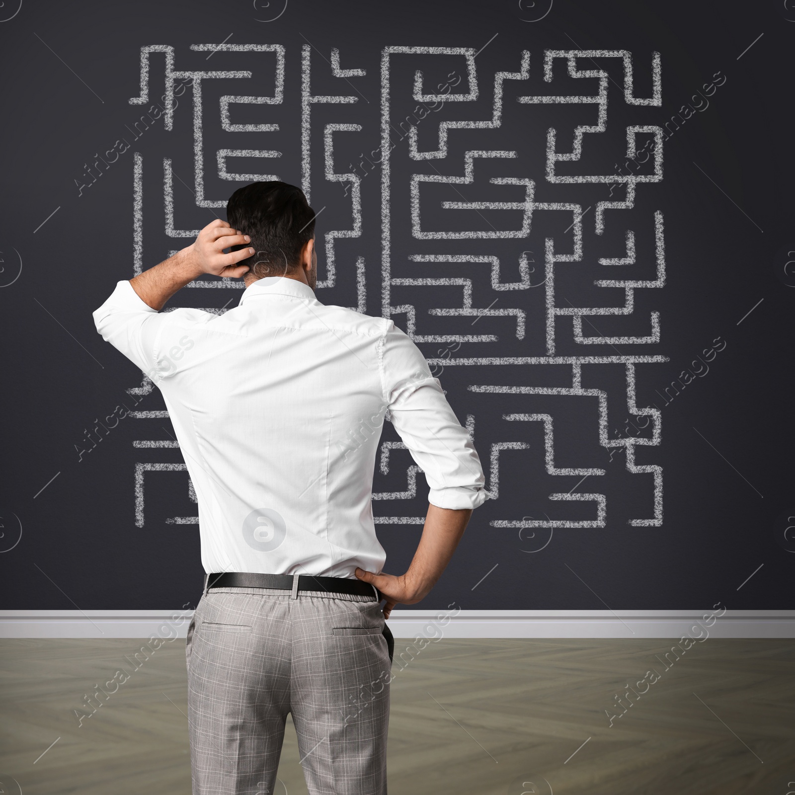 Image of Businessman looking at wall with illustration of maze indoors