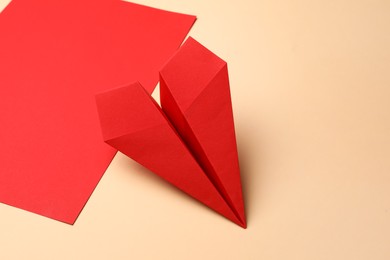Handmade red plane and piece of paper on beige background, space for text
