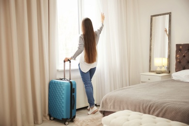 Photo of Young woman with luggage in hotel room