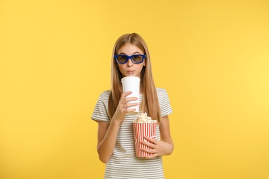 Emotional teenage girl with 3D glasses, popcorn and beverage during cinema show on color background