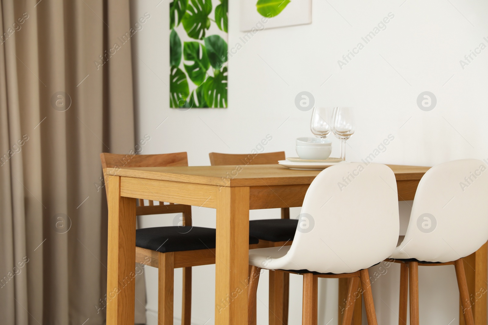 Photo of Stylish room interior with dining table and bar stools near white wall