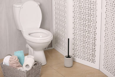 Photo of White toilet bowl near folding screen in bathroom