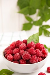 Photo of Bowl of fresh ripe raspberries with green leaf on white table, space for text