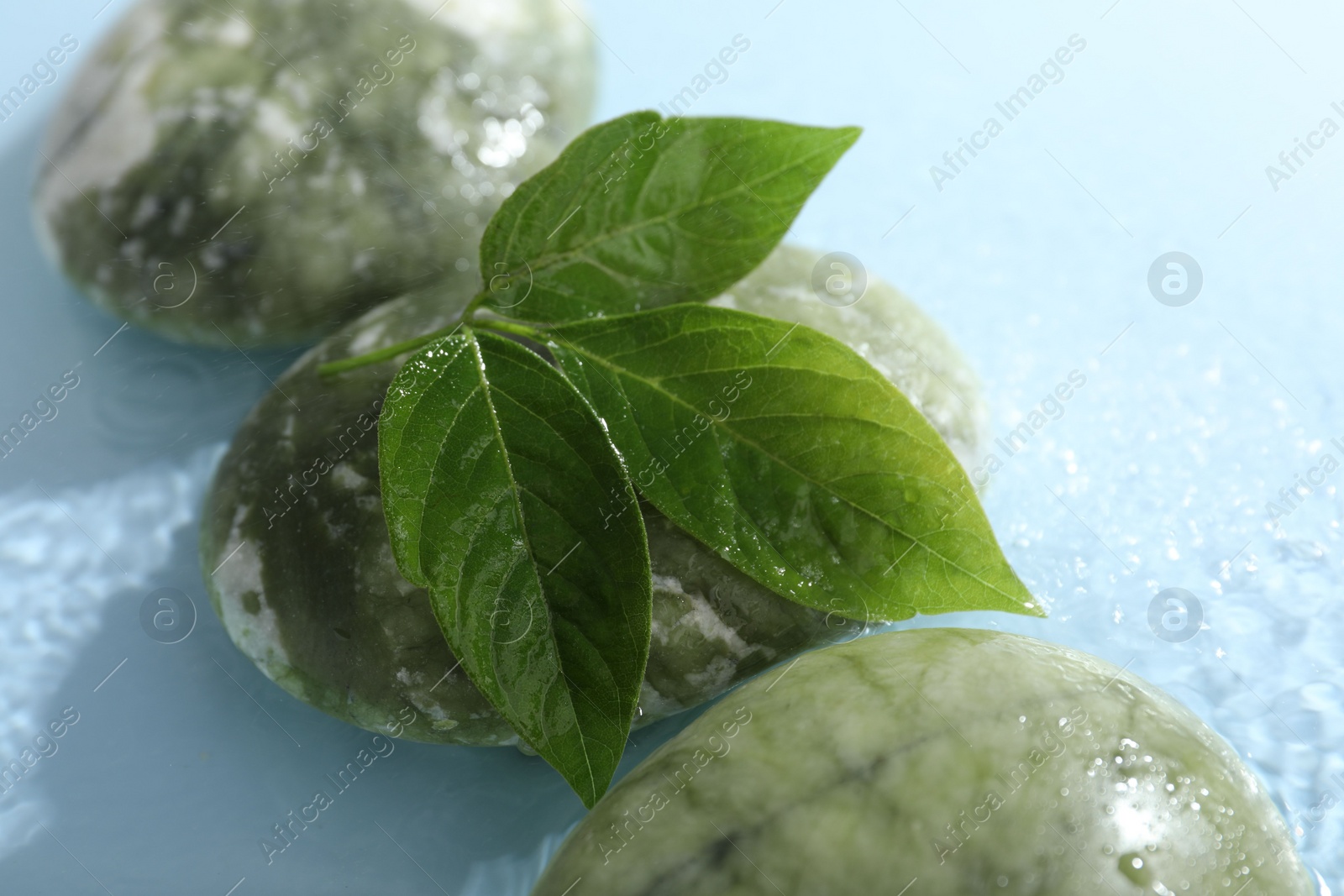 Photo of Spa stones and green leaves in water on light blue background, closeup