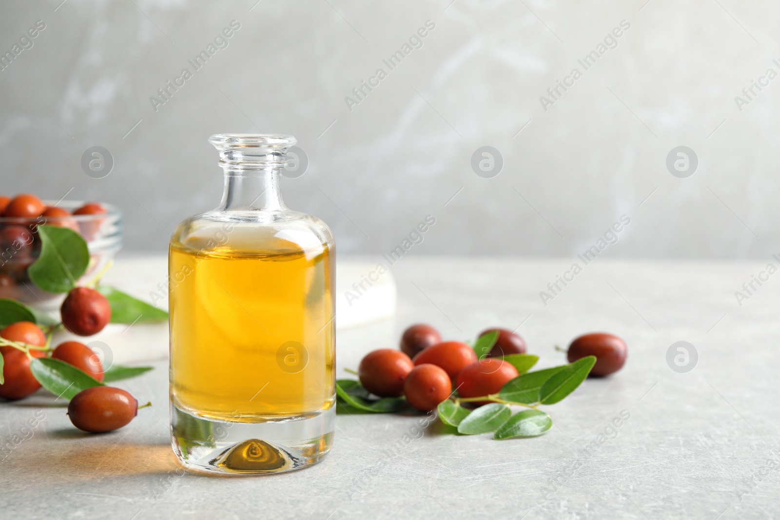 Photo of Jojoba oil in glass bottle and seeds on light grey table