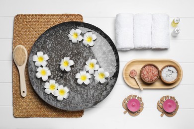 Photo of Bowl of water with flowers and different spa supplies on white wooden table, flat lay