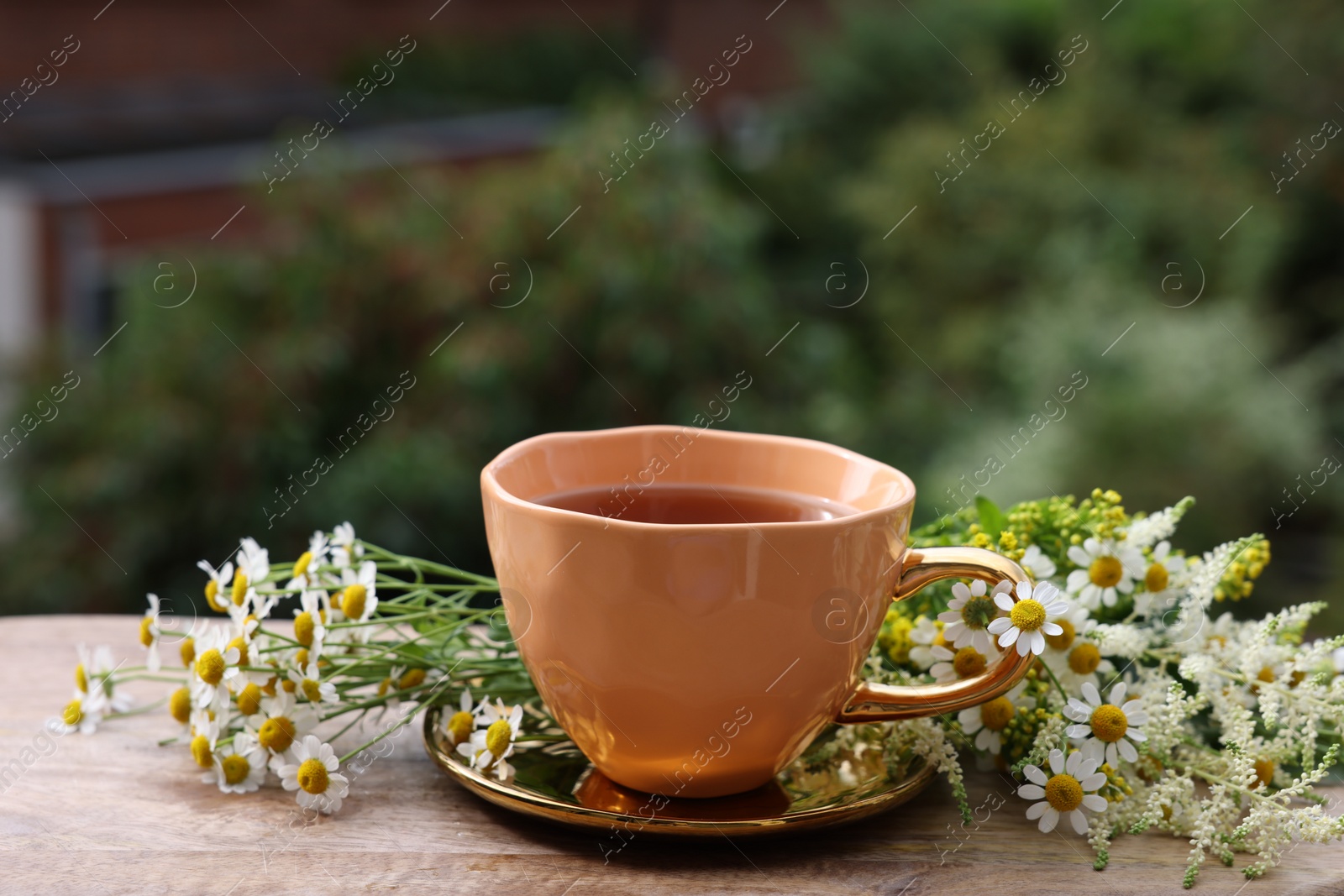 Photo of Cup of delicious chamomile tea and fresh flowers outdoors