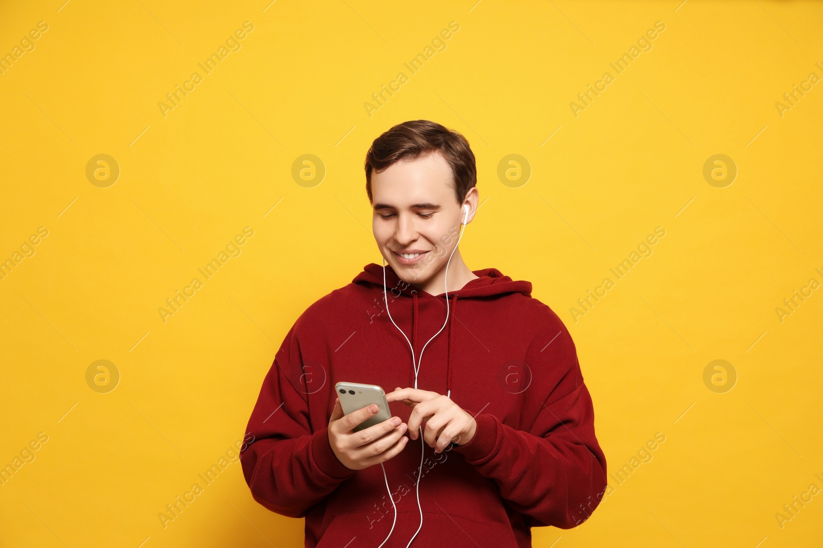 Photo of Handsome young man with earphones and smartphone on yellow background