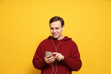 Photo of Handsome young man with earphones and smartphone on yellow background