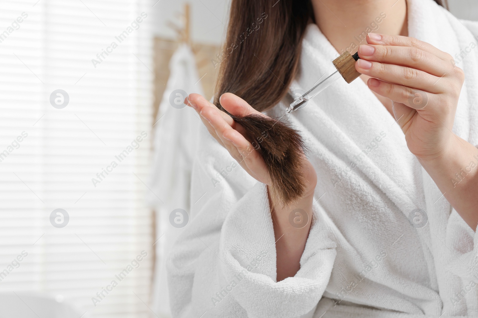 Photo of Woman applying essential oil onto hair indoors, closeup and space for text