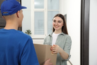 Photo of Courier giving parcel to young woman indoors