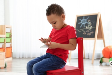 Photo of Cute little African-American child playing on mobile phone in kindergarten. Indoor activity