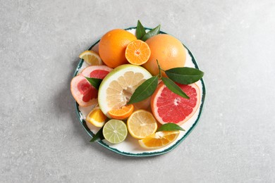 Plate with different citrus fruits and fresh leaves on light grey table, top view