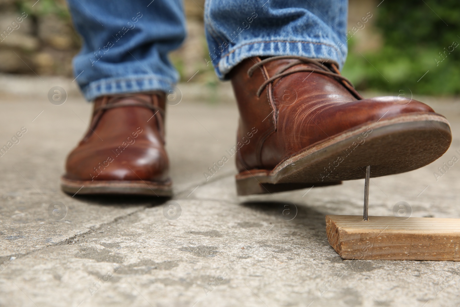 Photo of Careless man stepping on nail in wooden plank outdoors, closeup