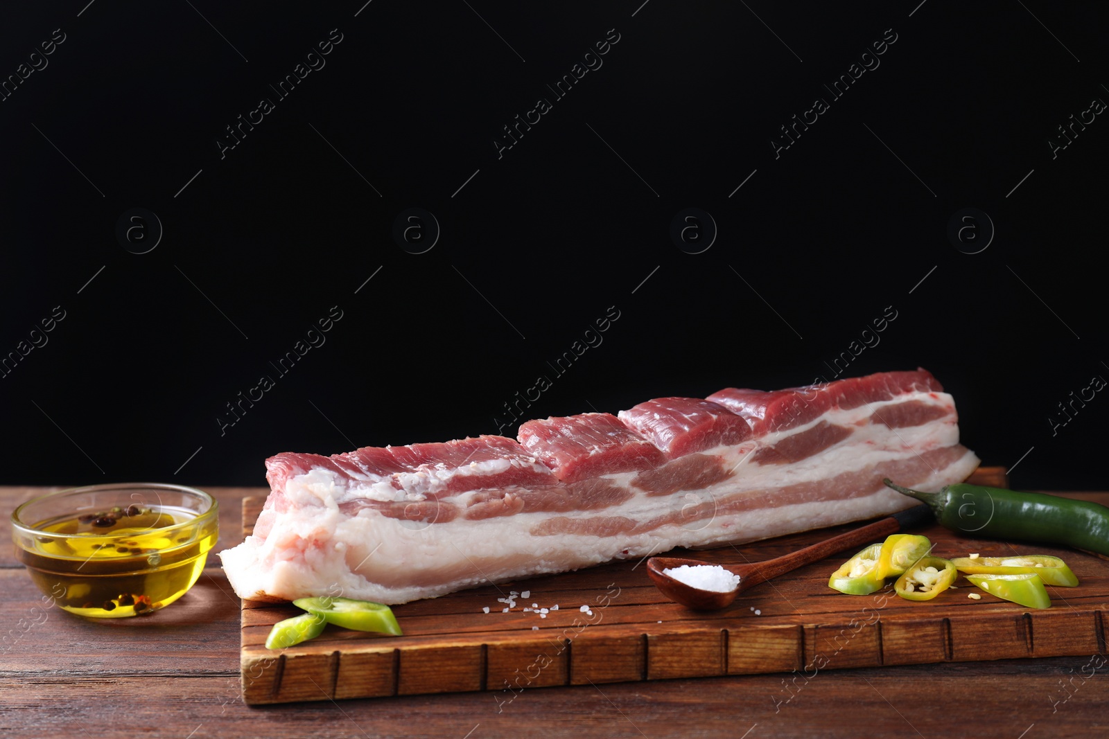 Photo of Piece of raw pork belly, green chili pepper, oil and salt on wooden table. Space for text