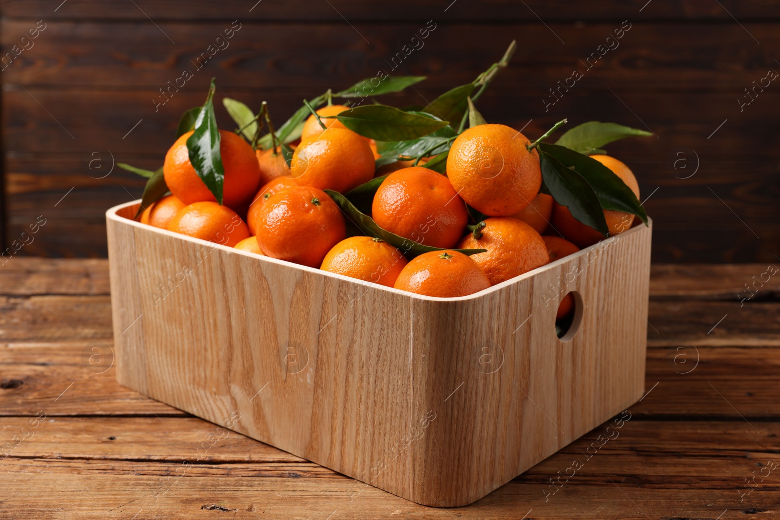 Photo of Fresh tangerines with green leaves in crate on wooden table