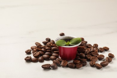 Photo of Coffee capsule with seedling and beans on white marble table. Space for text
