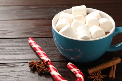 Photo of Tasty hot chocolate with marshmallows, candy cane and spices on wooden table, closeup. Space for text