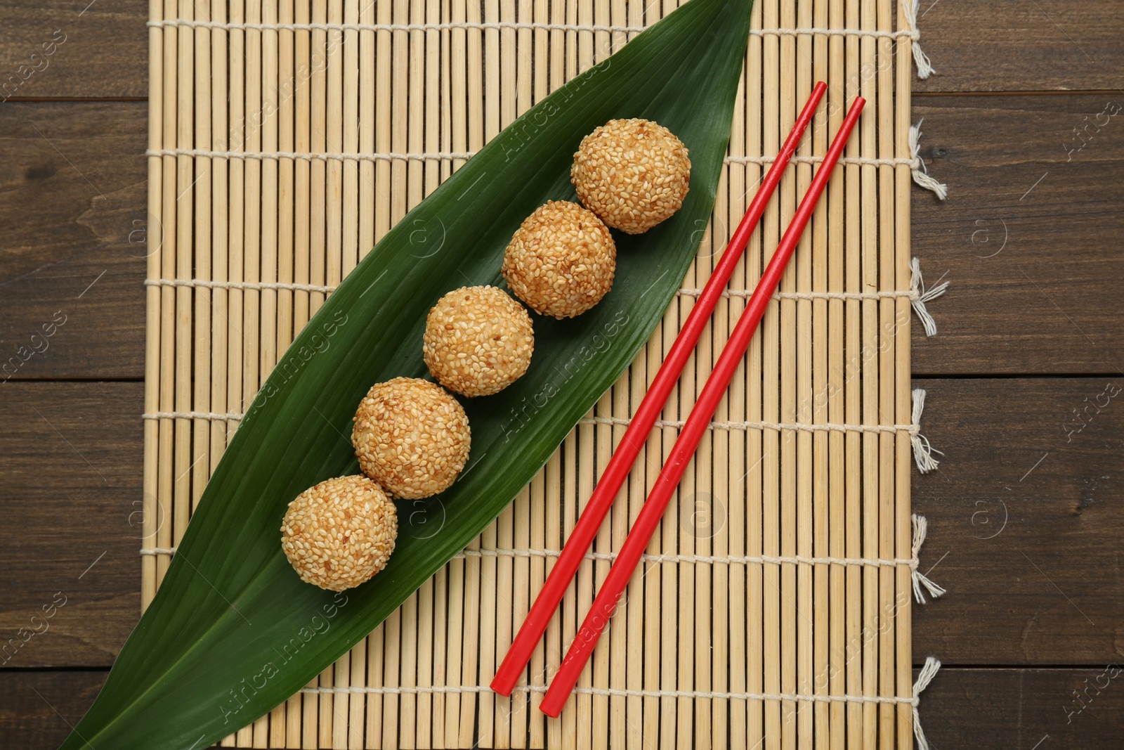 Photo of Delicious sesame balls, green banana leaf and chopsticks on wooden table, flat lay
