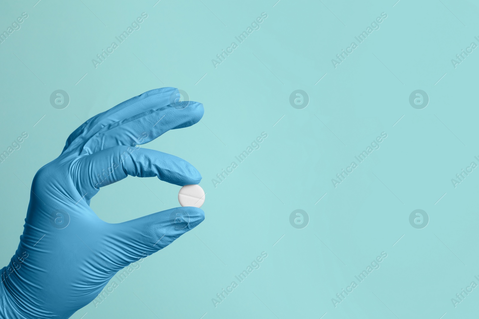 Photo of Doctor holding pill on turquoise background, closeup. Space for text