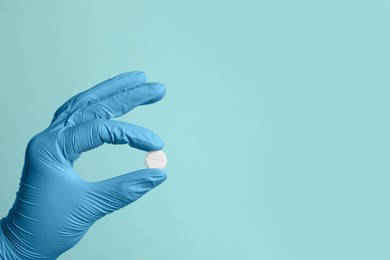 Doctor holding pill on turquoise background, closeup. Space for text