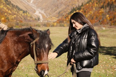 Young woman stroking horse in mountains on sunny day. Beautiful pet