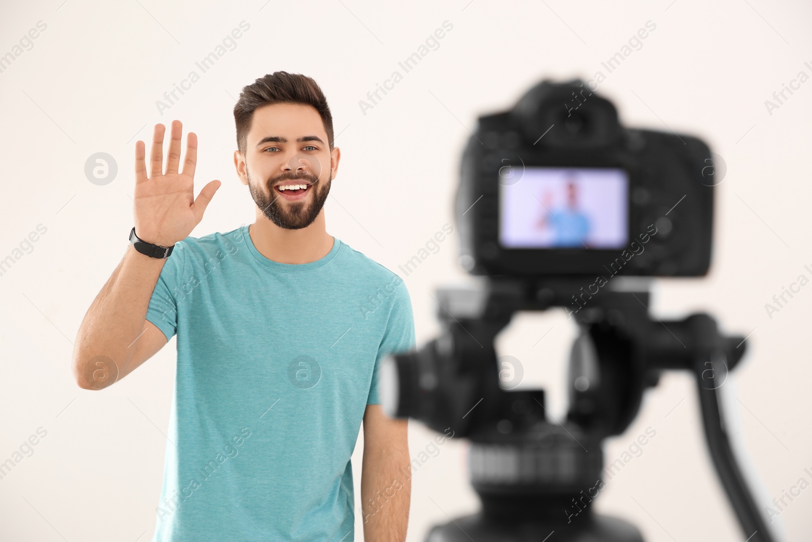 Photo of Young blogger recording video on camera against white background