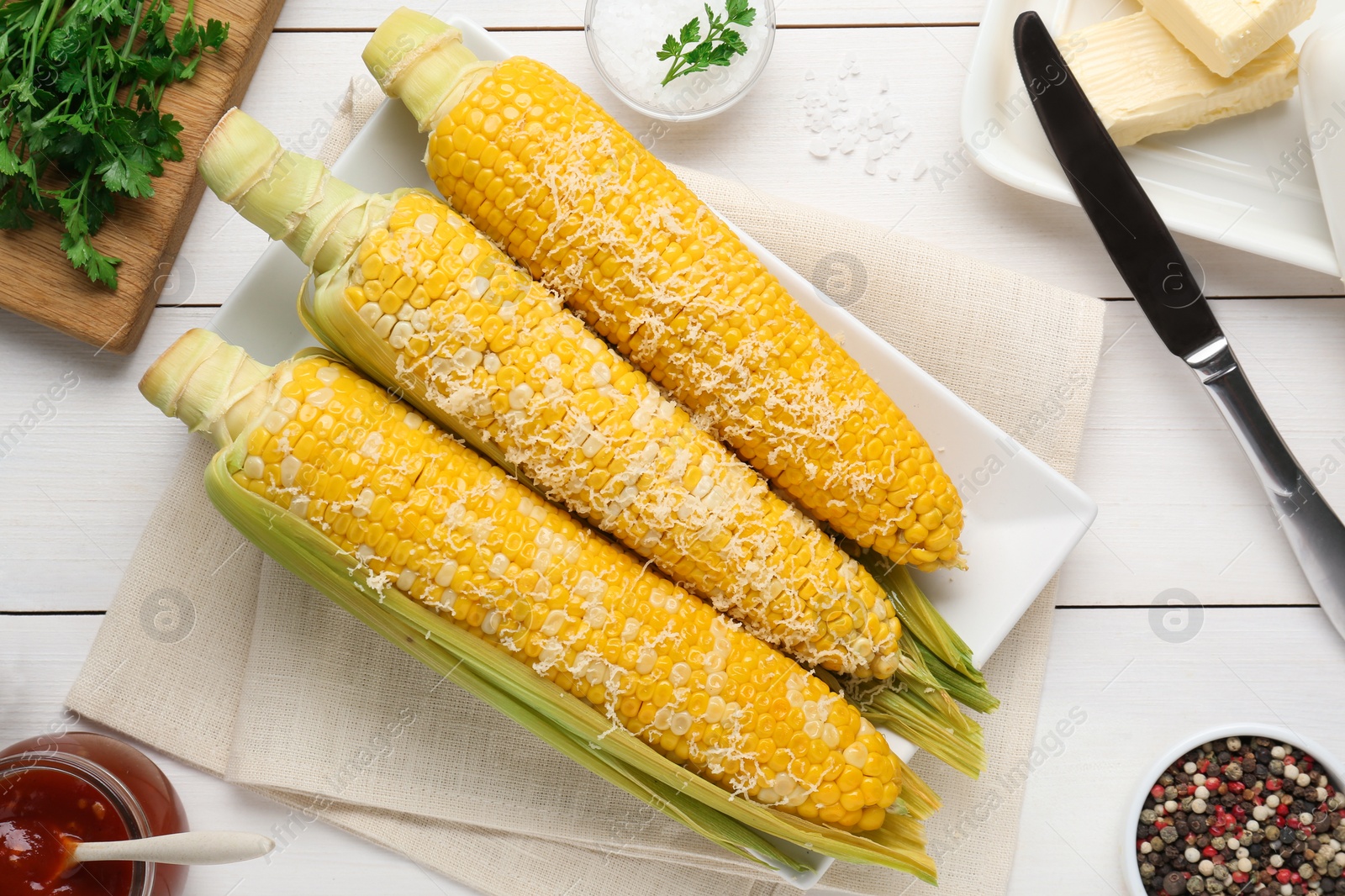 Photo of Plate with tasty cooked corn cobs on white wooden table, flat lay
