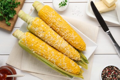 Plate with tasty cooked corn cobs on white wooden table, flat lay
