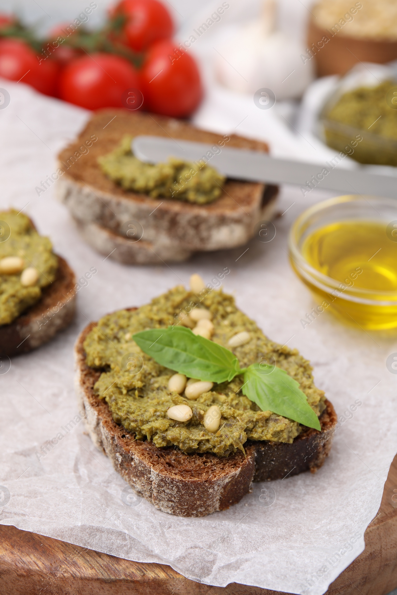 Photo of Tasty bruschettas with pesto sauce, nuts and fresh basil on wooden board, closeup