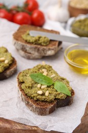 Tasty bruschettas with pesto sauce, nuts and fresh basil on wooden board, closeup