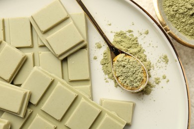 Pieces of tasty matcha chocolate bar and powder in spoon on table, top view