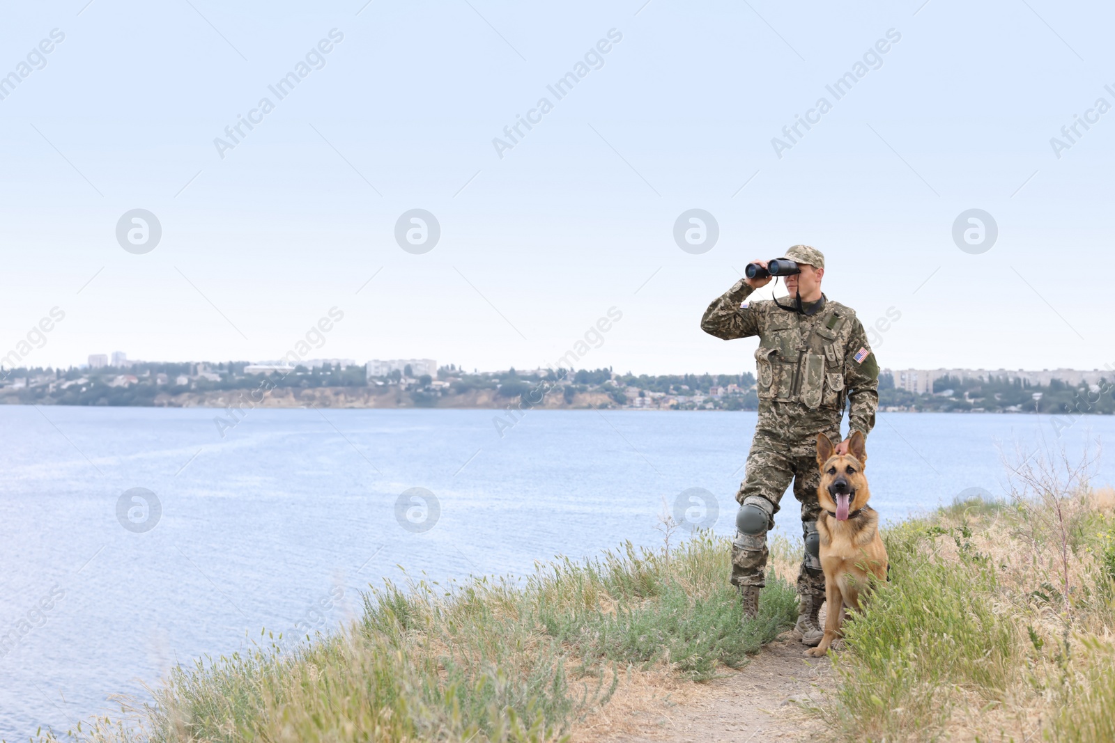 Photo of Man in military uniform with German shepherd dog near river