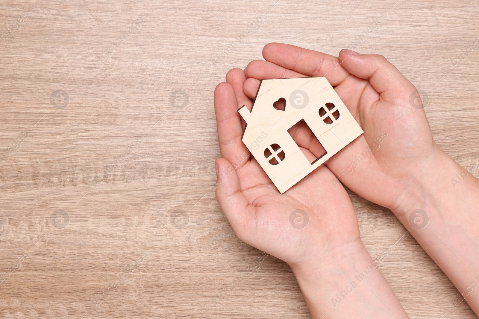 Photo of Home security concept. Man holding house model at wooden table, top view with space for text