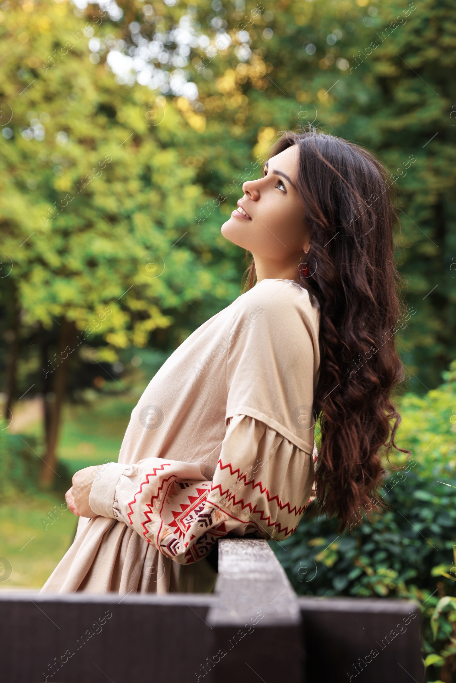 Photo of Beautiful woman wearing embroidered dress near wooden railing in countryside. Ukrainian national clothes