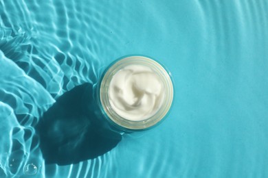 Photo of Jar with moisturizing cream in water on light blue background, top view